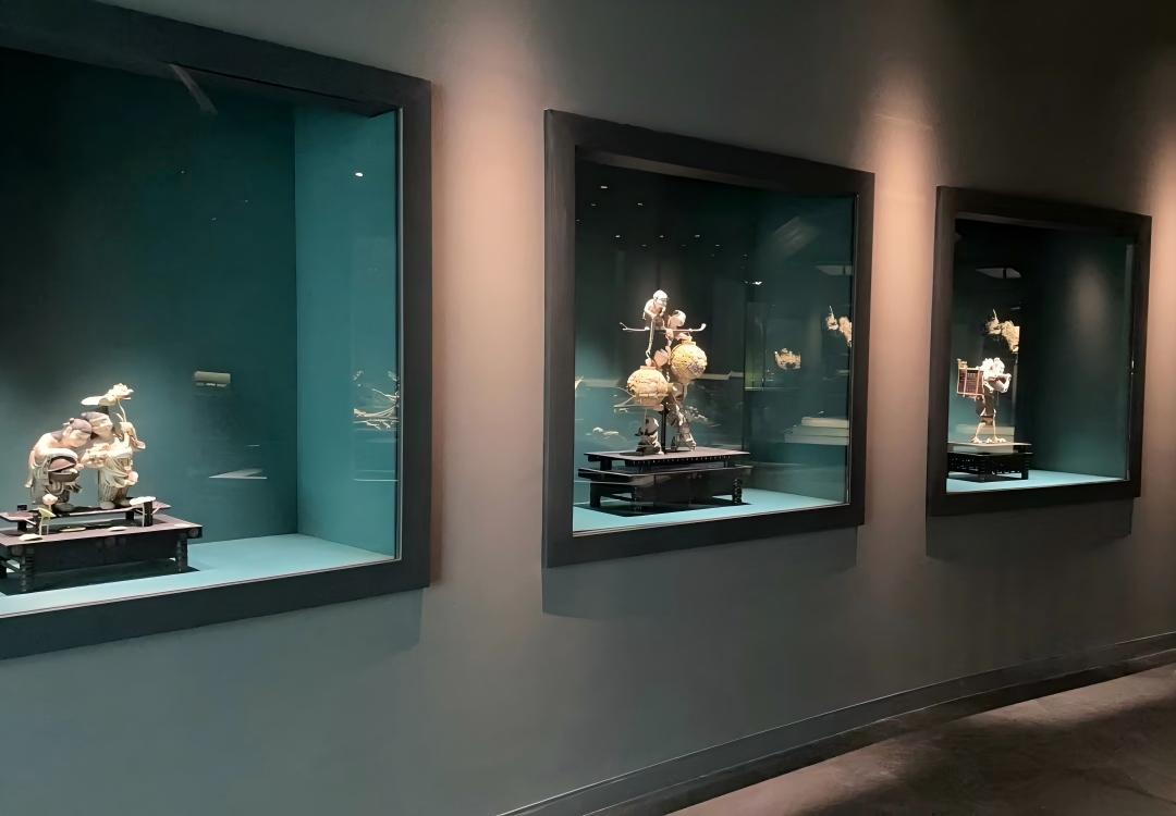 Row of recessed built‑in wall museum display cases exhibiting delicate carved cultural relic sculptures inside gallery
