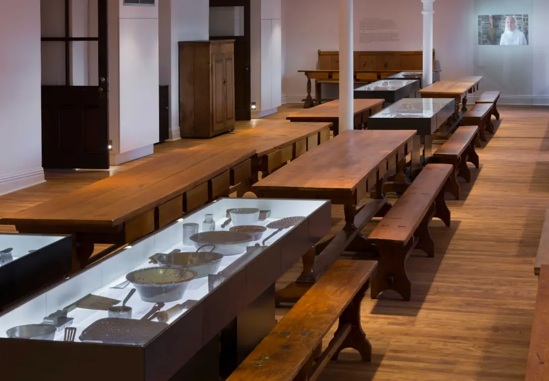 Long low glass museum display cases with internal lighting showcasing antique kitchen artifacts in historic exhibition hall