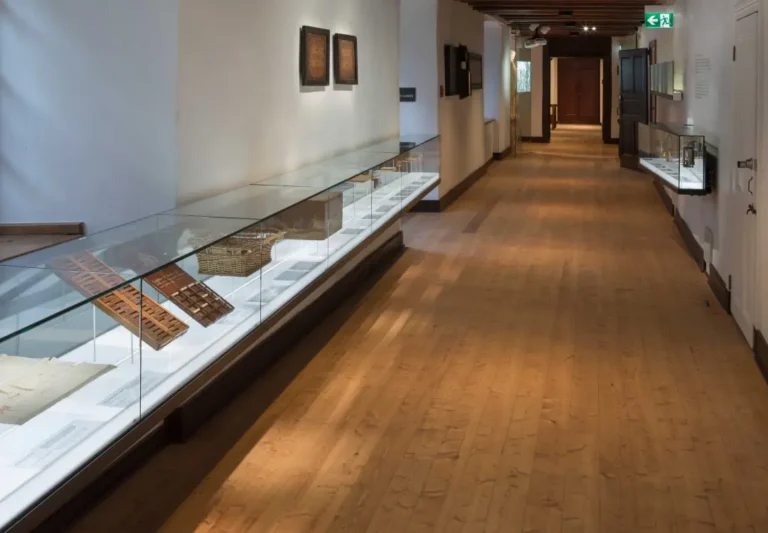 Continuous wall mounted glass display cabinets for old wooden artifacts along warm wooden floor museum corridor