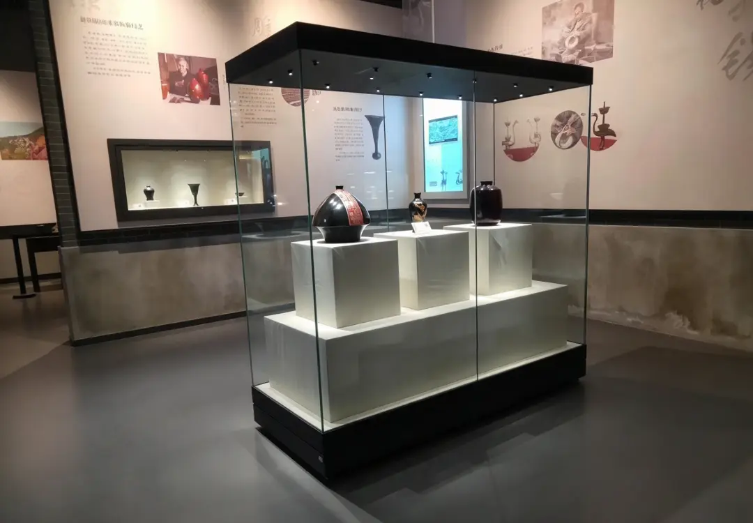 Freestanding museum vitrines with tiered white pedestals displaying antique ceramic artworks and built-in spotlights